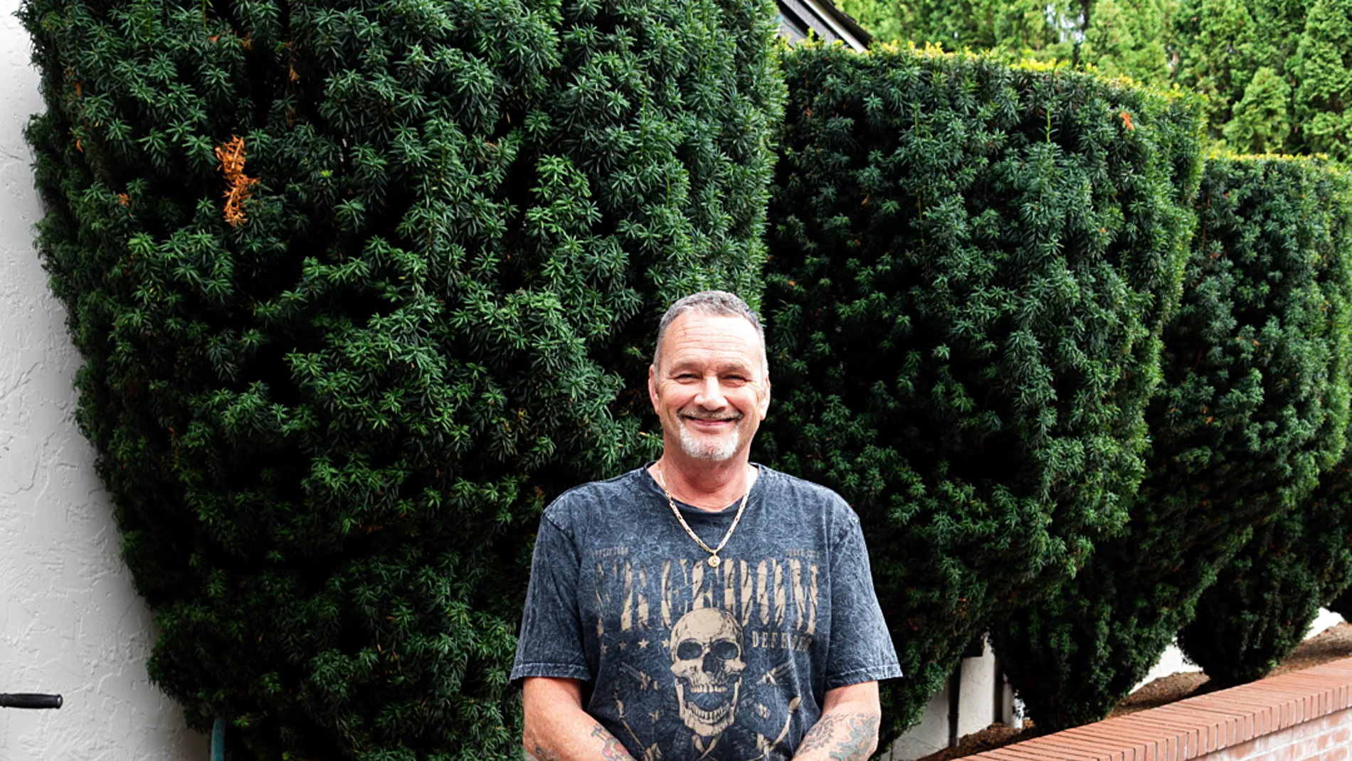 John Speaks, owner, smiling in front of a hedge