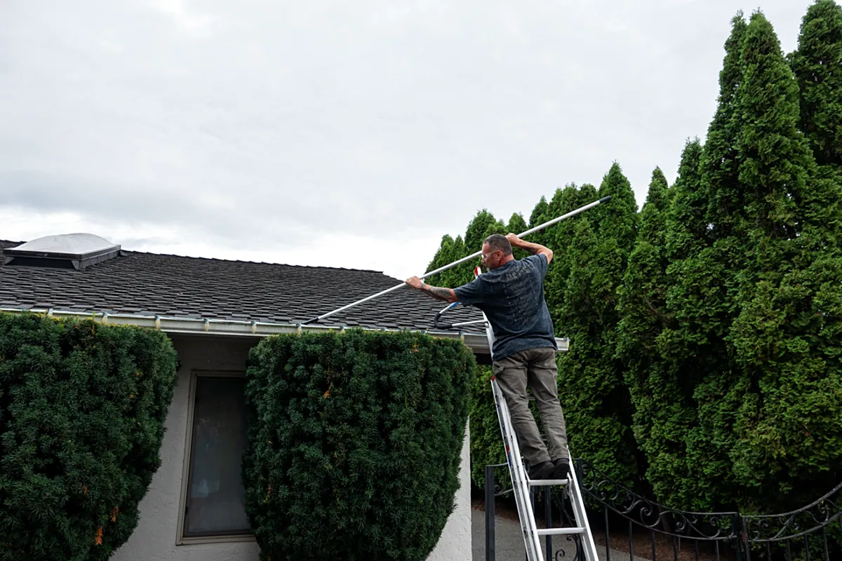 John clearing a gutter with an extension pole from a ladder